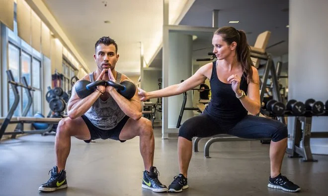 Veronika coaching a kettlebell squat in a gym